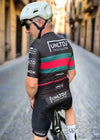 Cyclist wearing a black cycling outfit with visible branding on a road.