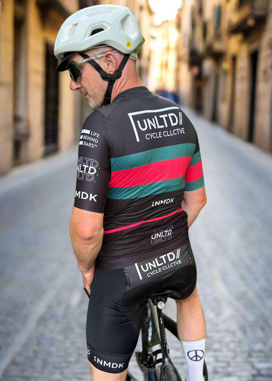 Cyclist wearing a black cycling outfit with visible branding on a road.